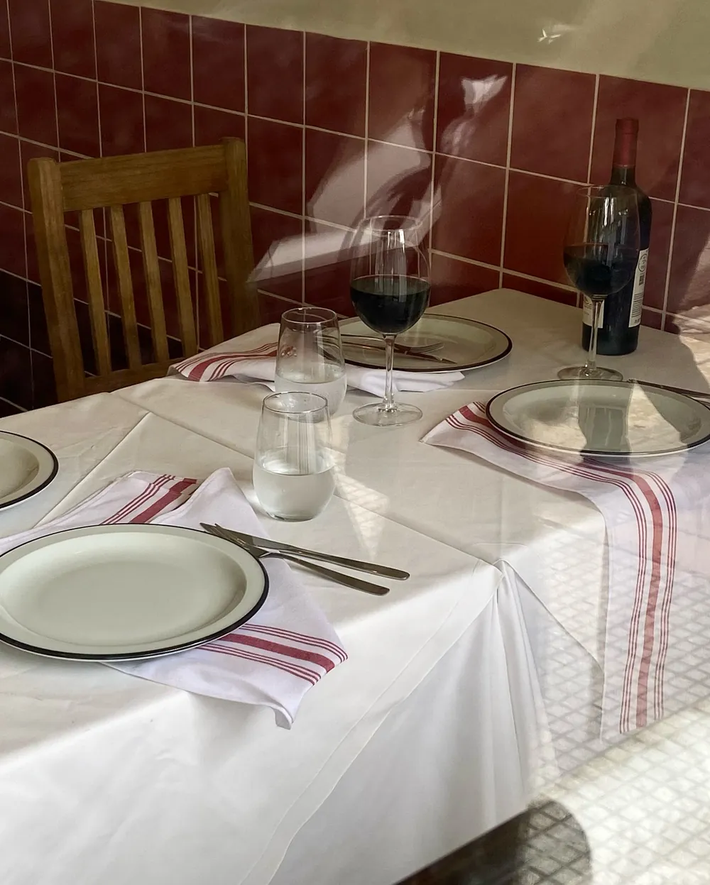 Mesa puesta con mantel blanco, servilletas a rayas y vino tinto